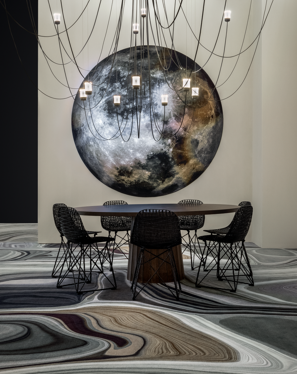 mooon carpet on the wall with gravity chandelier and container table setting with carbon chairs